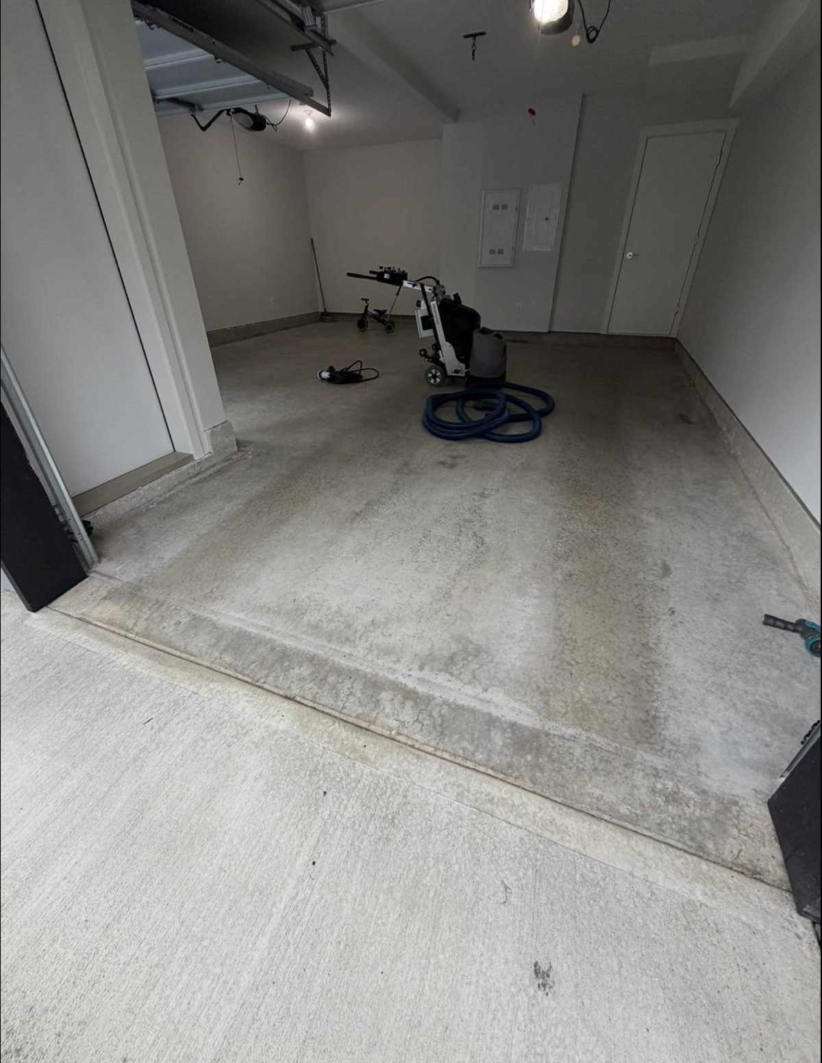 Before: stained, dusty bare concrete garage floor in a Sullivan Square townhome in Surrey, mid-prep with a floor grinder